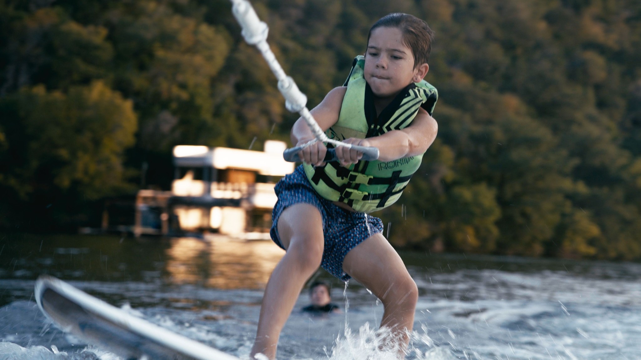 Wakesurfer riding boat wake in crystal clear lake water, boat visible